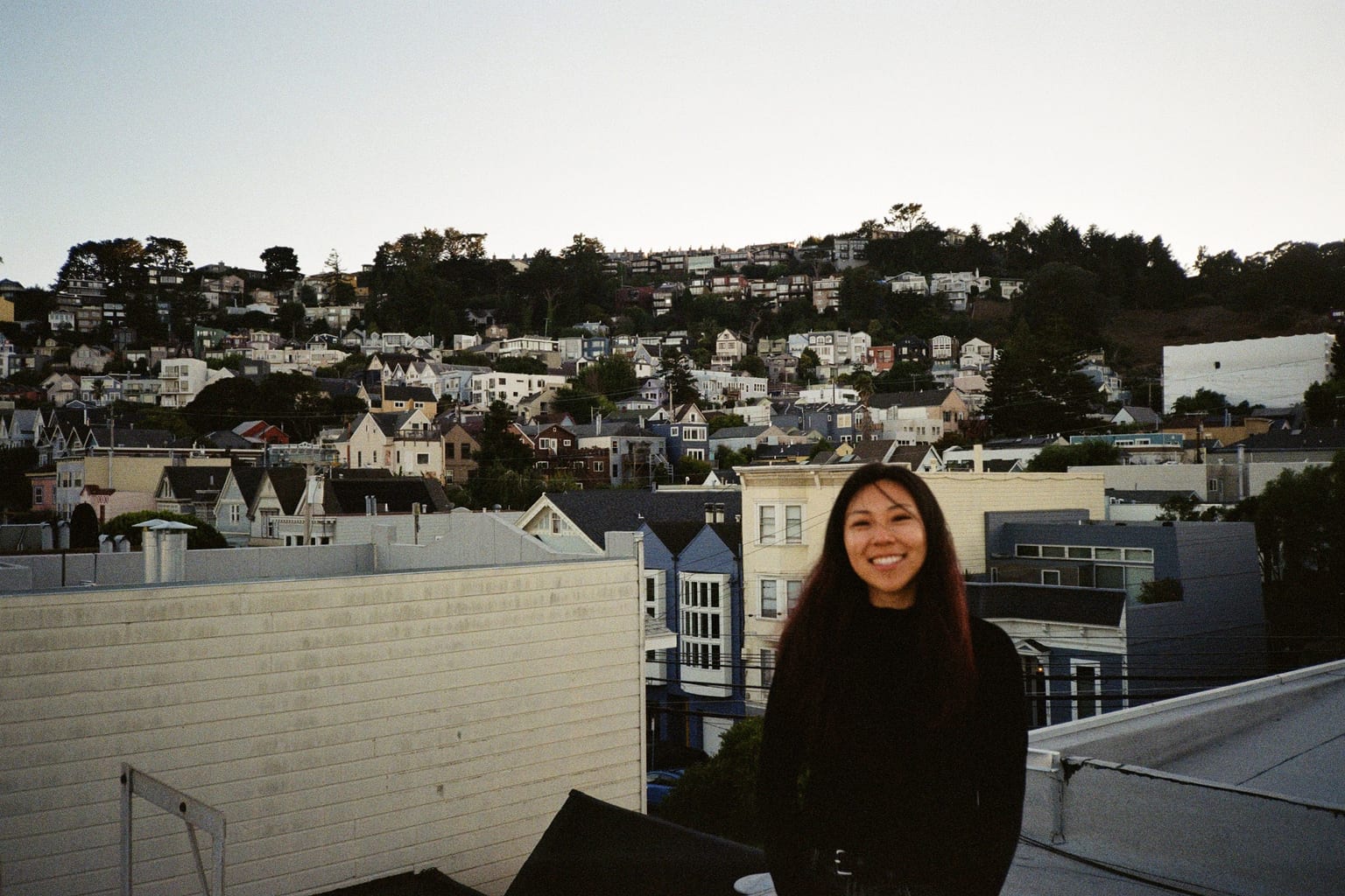 Stephanie standing on a rooftop at dusk, with the hills of San Francisco rising behind her